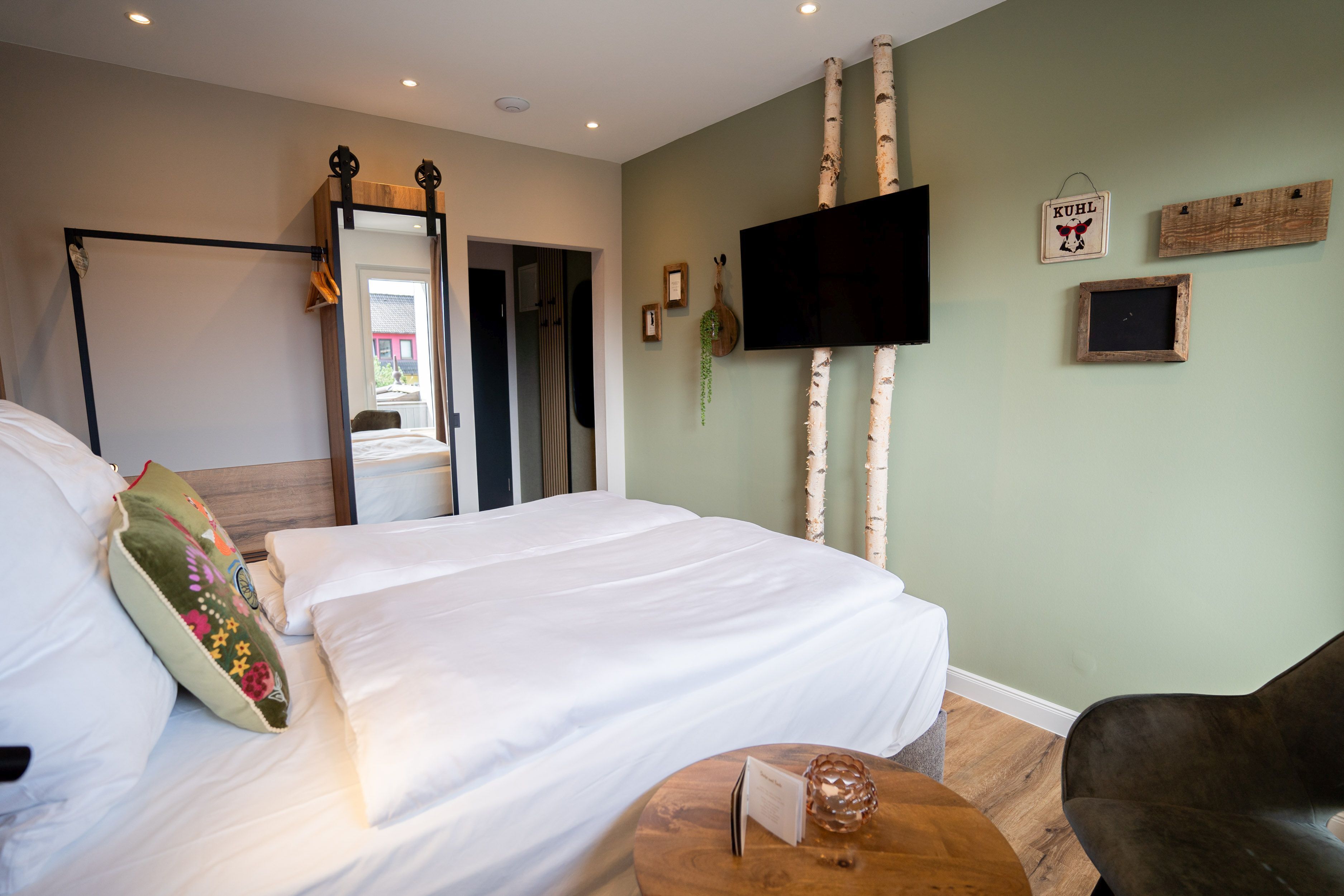 A hotel room with a bed, a round wooden table, a television, and a mirror.