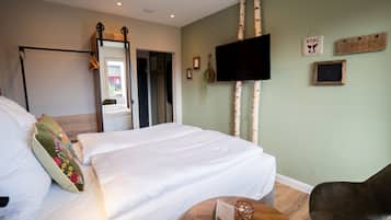 Una camera d'albergo con un letto, un tavolino rotondo in legno, una televisione e uno specchio.