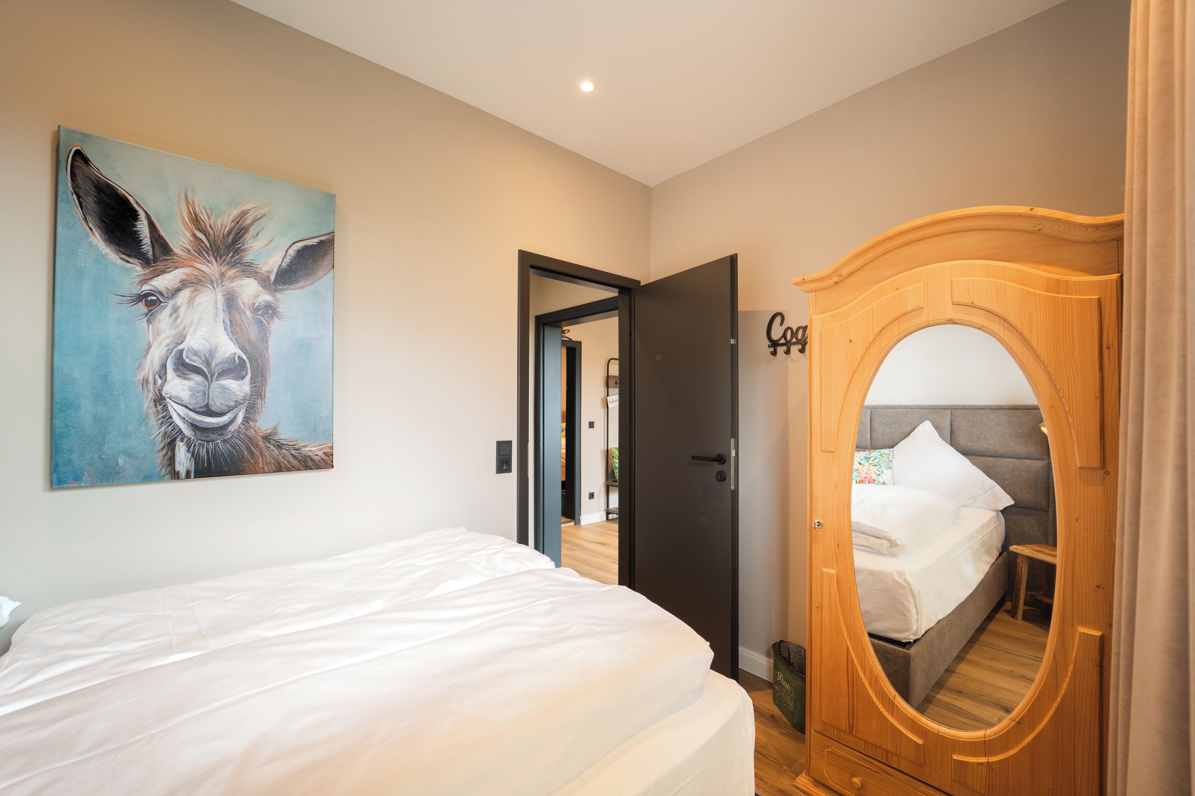 Una camera da letto con un letto, un armadio in legno, uno specchio e un quadro raffigurante un cavallo al muro.
