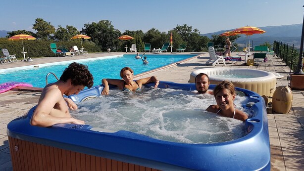 A hot tub with people around it, a pool, and lounge chairs with umbrellas. - Apartment in Poppi With Shared Pool (Poppi)