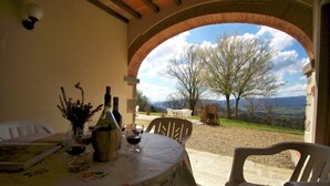 An outdoor dining area with a table set for two, a view of the countryside, and a brick archway. - Apartment in Poppi With Shared Pool (Poppi)