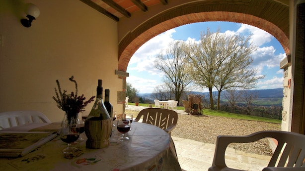 An outdoor dining area with a table set for two, a view of the countryside, and a brick archway. - Apartment in Poppi With Shared Pool (Poppi)