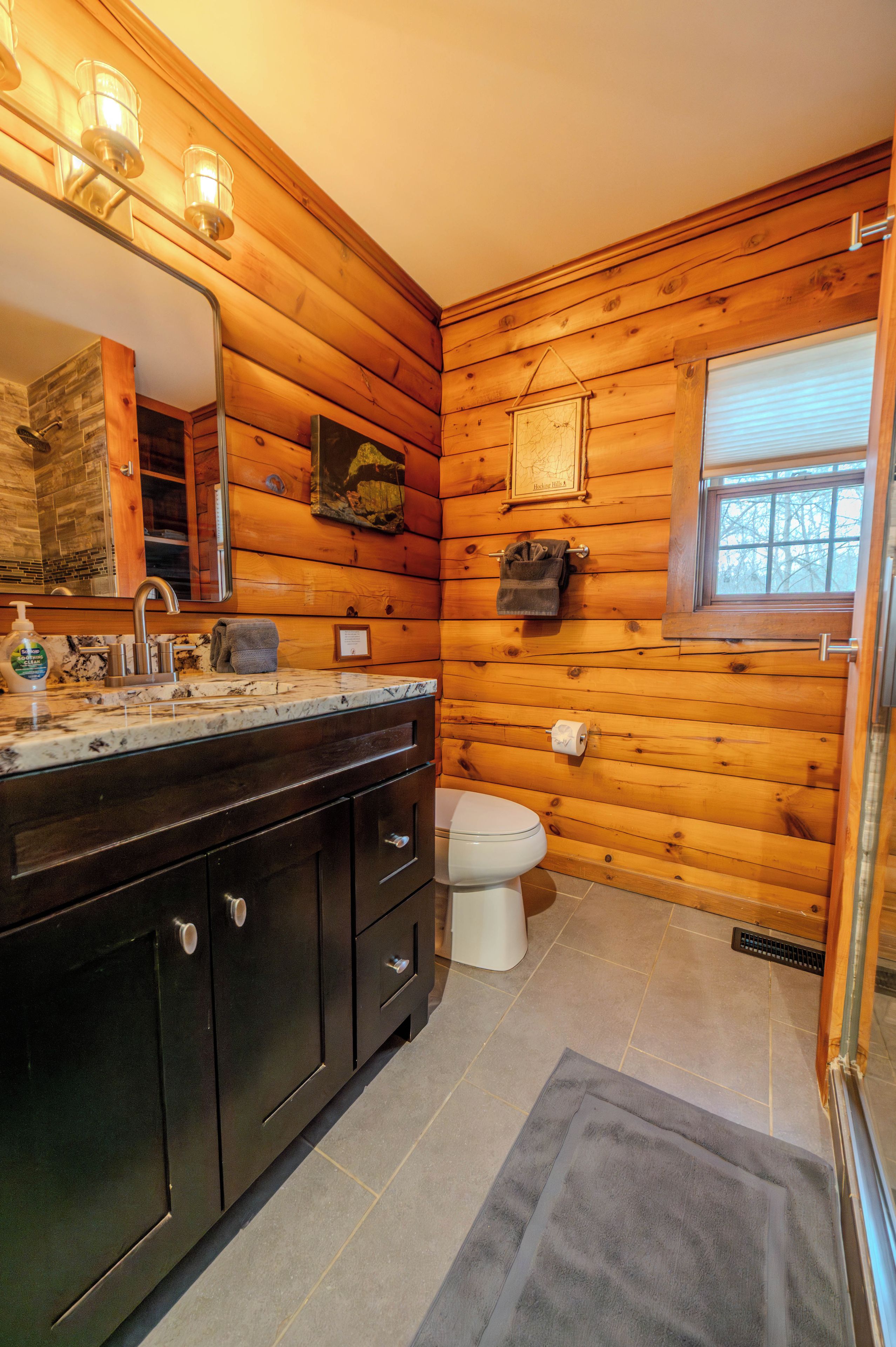 A wooden cabin bathroom with a sink, mirror, towel rack, and toilet.