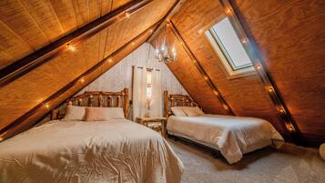 Une chambre mansardée avec deux lits, des poutres en bois, un puits de lumière et des guirlandes lumineuses.