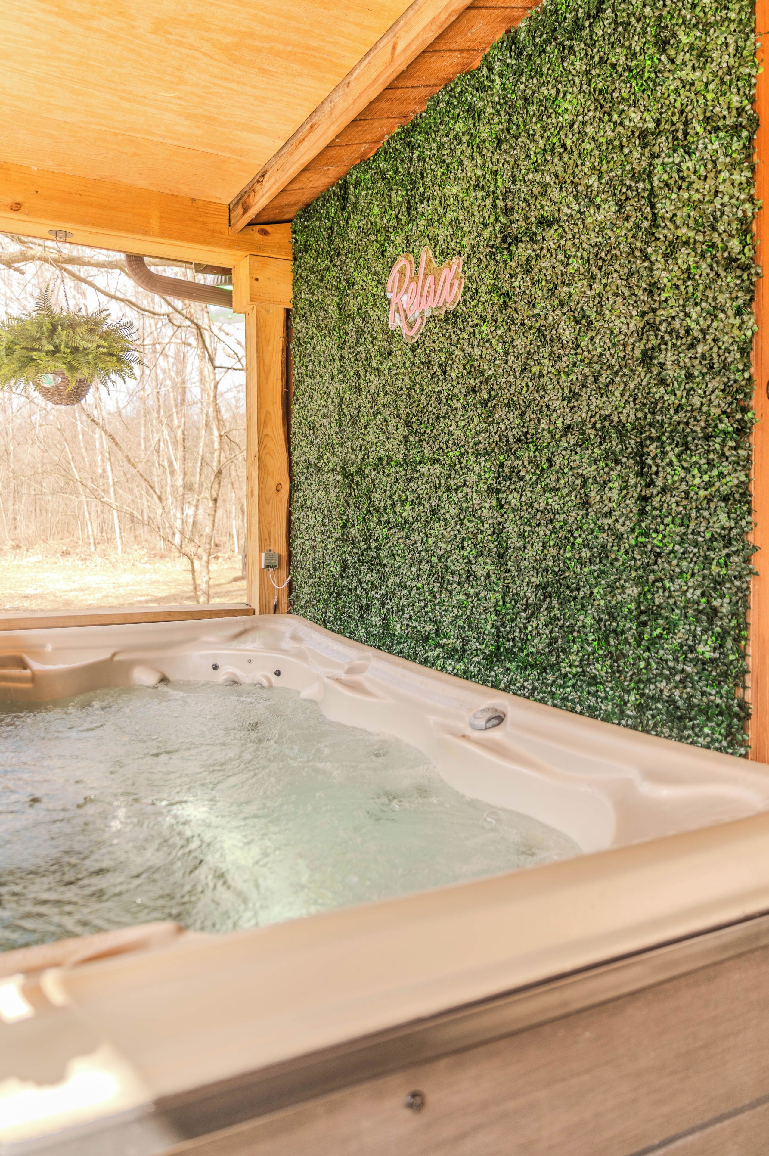 Un bain à remous doté d’un plafond en bois et d’un mur recouvert de feuillage verdoyant.