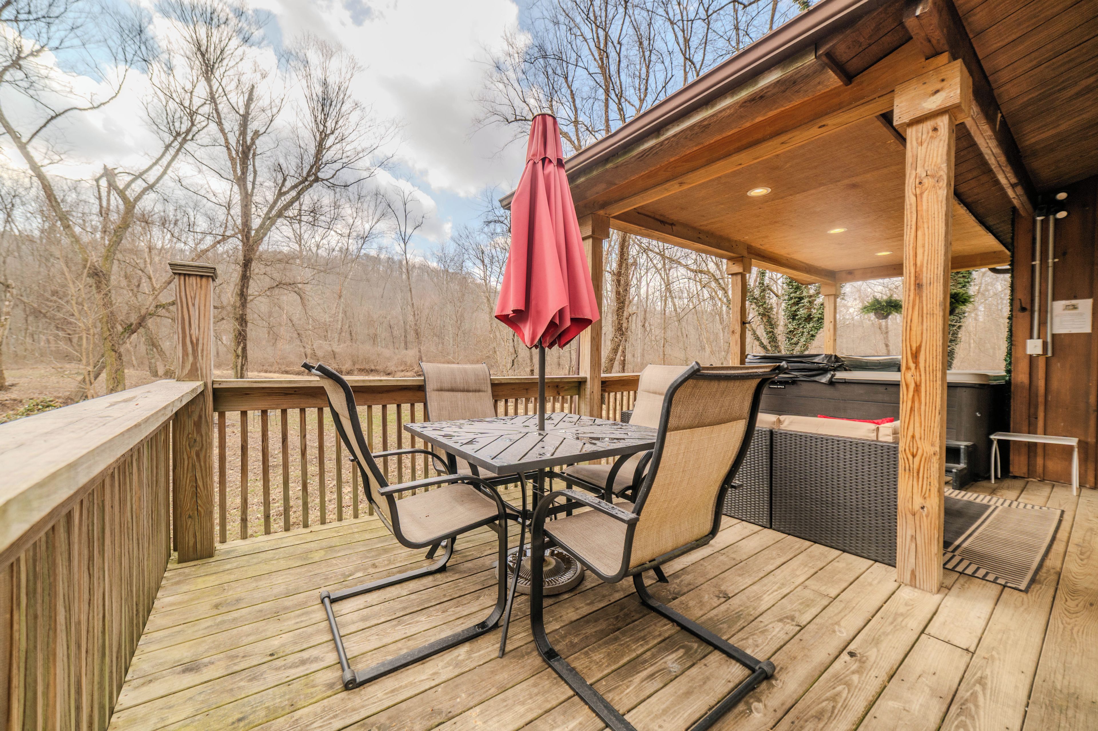 A wooden deck with a metal table and chairs, a red umbrella, and a barbecue grill.