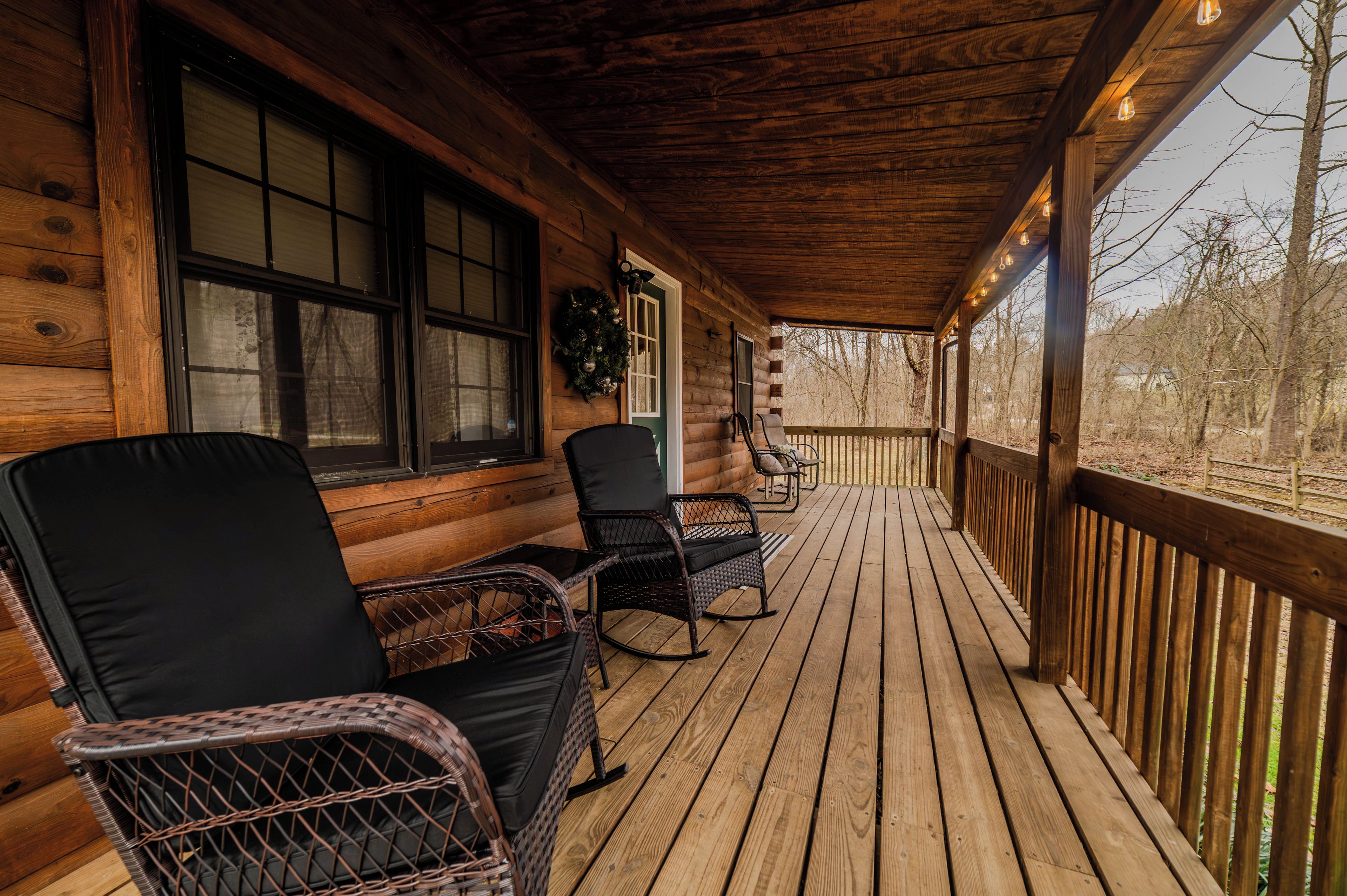 A wooden porch with wicker chairs and a bench, overlooking a wooded area.