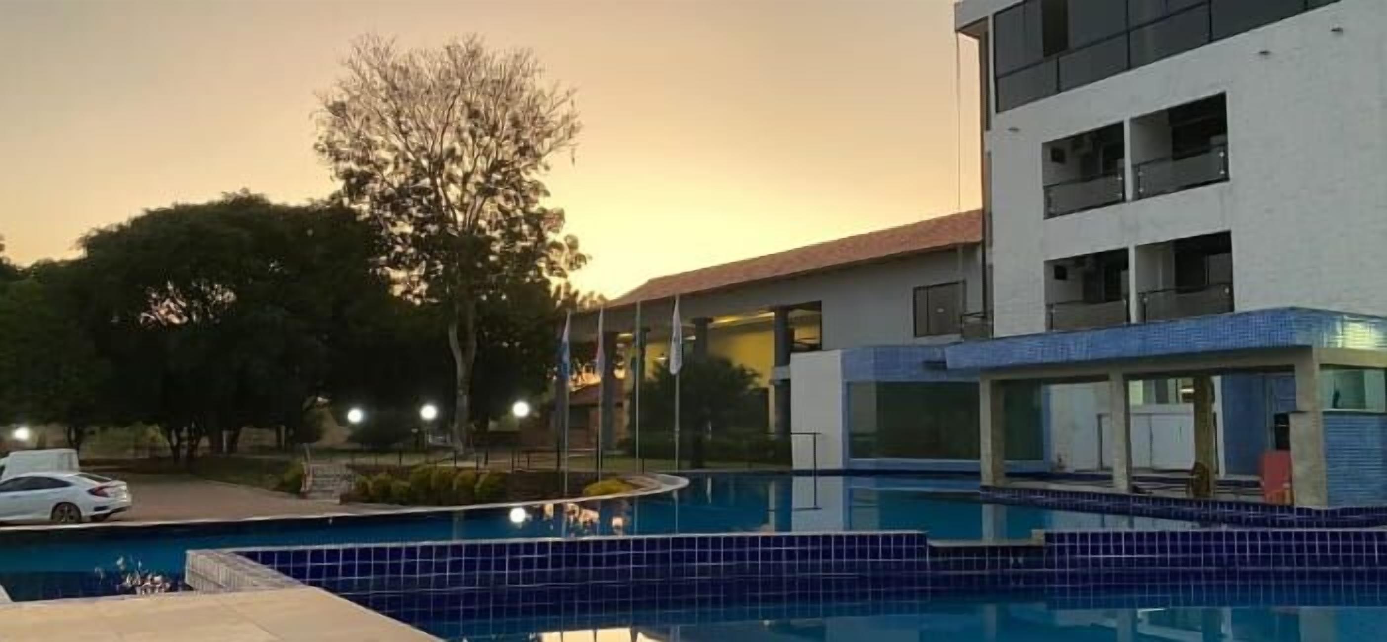 A modern building with a swimming pool, surrounded by trees and a parked car.
