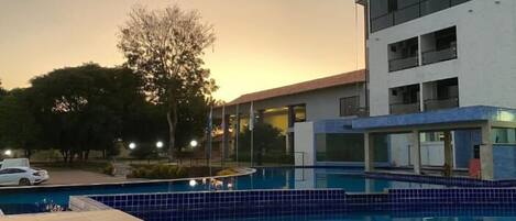 A modern building with a swimming pool, surrounded by trees and a parked car.
