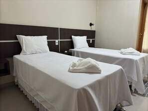 Ein Hotelzimmer mit zwei Einzelbetten, jeweils mit weißer Bettdecke und Kissen, einem dunklen Holz-Kopfteil, einem Nachttisch mit Telefon und einem gefalteten Handtuch auf dem Bett.
