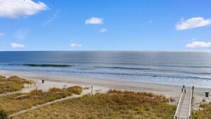A beach with a wooden walkway leading to the water, a clear sky, and a calm sea.