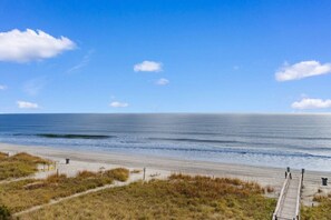 A beach with a wooden walkway leading to the water, a clear sky, and a calm sea.