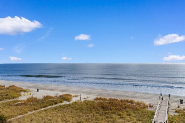 Een strand met een houten looppad naar het water, een heldere lucht en een rustige zee.