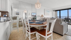 A modern interior with a dining area, kitchen, and living space, featuring a large window and a balcony.