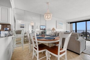 A modern interior with a dining area, kitchen, and living space, featuring a large window and a balcony.
