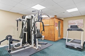 A gym with various exercise equipment, a treadmill, and a wooden cabinet.