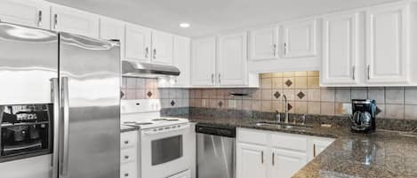 A modern kitchen with stainless steel appliances, white cabinetry, and a granite countertop.