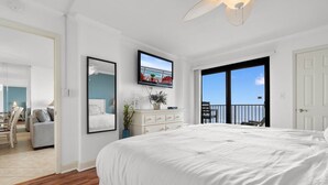 A bedroom with a large bed, a television, a dresser, and a balcony with a view.
