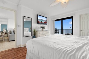 A bedroom with a large bed, a television, a dresser, and a balcony with a view.