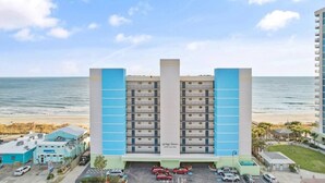 A hotel with multiple floors, a parking lot, and a beach view.
