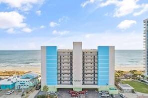 A hotel with multiple floors, a parking lot, and a beach view.
