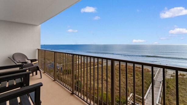 A balcony with a view of the ocean, a chair, and a wooden deck.