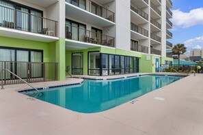 Un hotel con piscina, varios balcones y fachada verde.