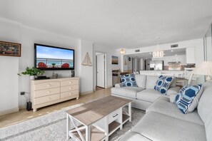 Un salon moderne avec un téléviseur à écran plat, un canapé beige et une table basse.