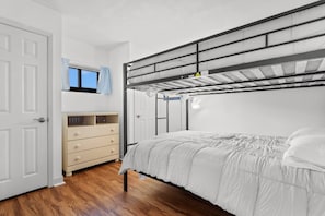 A bunk bed with a headboard, a bedside table, a dresser, and a window with curtains.