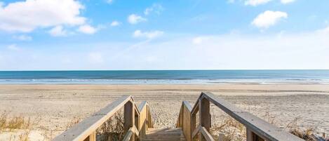 A wooden boardwalk leading to a beach with a clear sky.