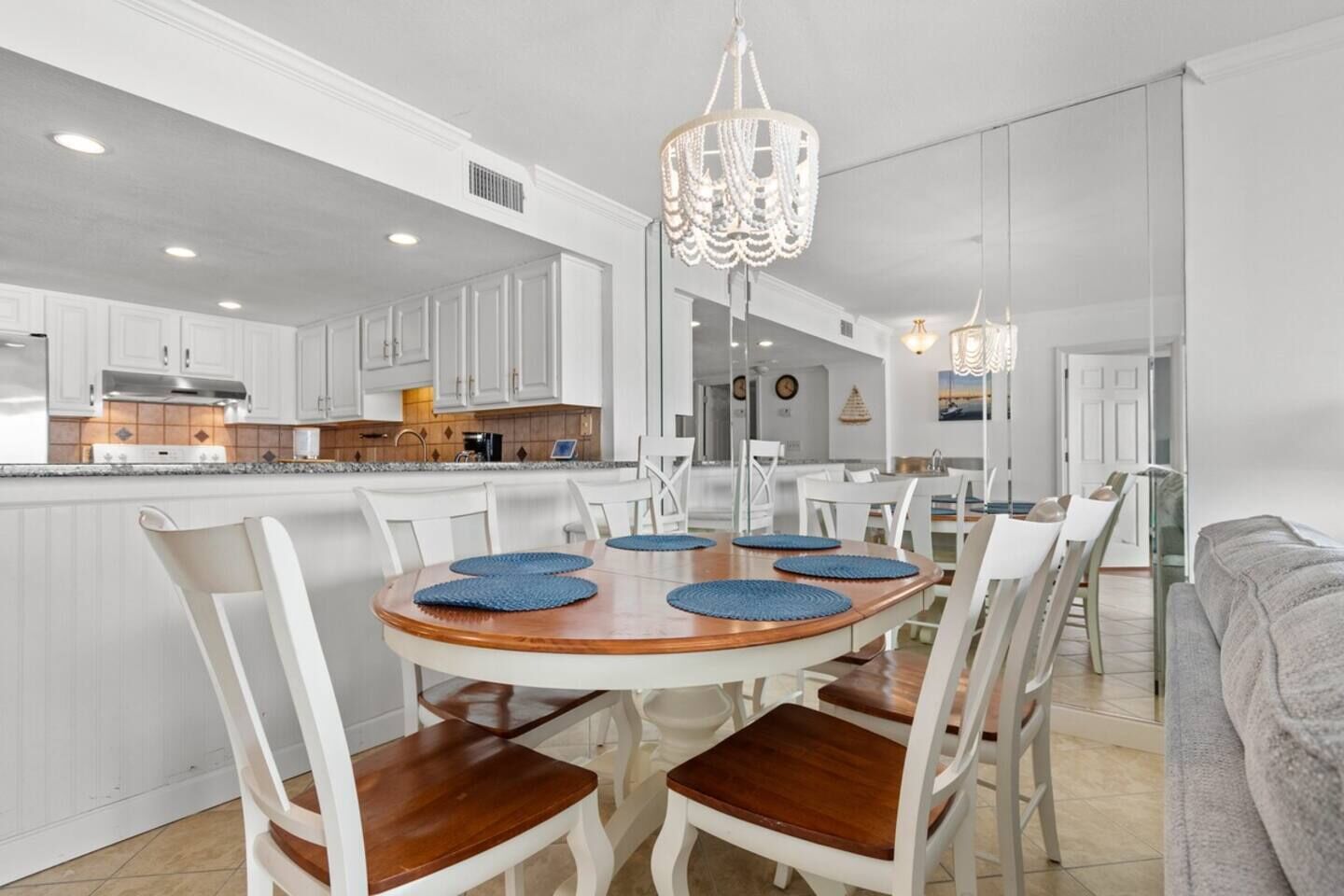 A modern kitchen with white cabinetry, a wooden dining table with blue placemats, and a chandelier.