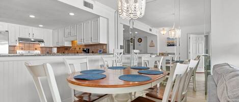 A modern kitchen with white cabinetry, a wooden dining table with blue placemats, and a chandelier.