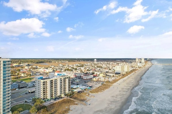 A coastal cityscape with high-rise buildings, a beach, and a clear sky.