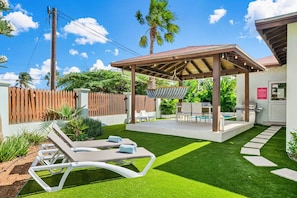 A backyard with a covered seating area, a pool, and a well-maintained lawn. - Backyard Bliss: 4BR Pool Home, 4Min to Eagle Beach (Noord)