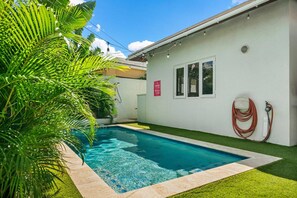 A swimming pool with a clear blue water, surrounded by artificial grass and a white building with a window and a hose. - Backyard Bliss: 4BR Pool Home, 4Min to Eagle Beach (Noord)