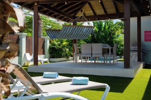 A covered outdoor area with lounge chairs and a dining table, surrounded by greenery. - Backyard Bliss: 4BR Pool Home, 4Min to Eagle Beach (Noord)