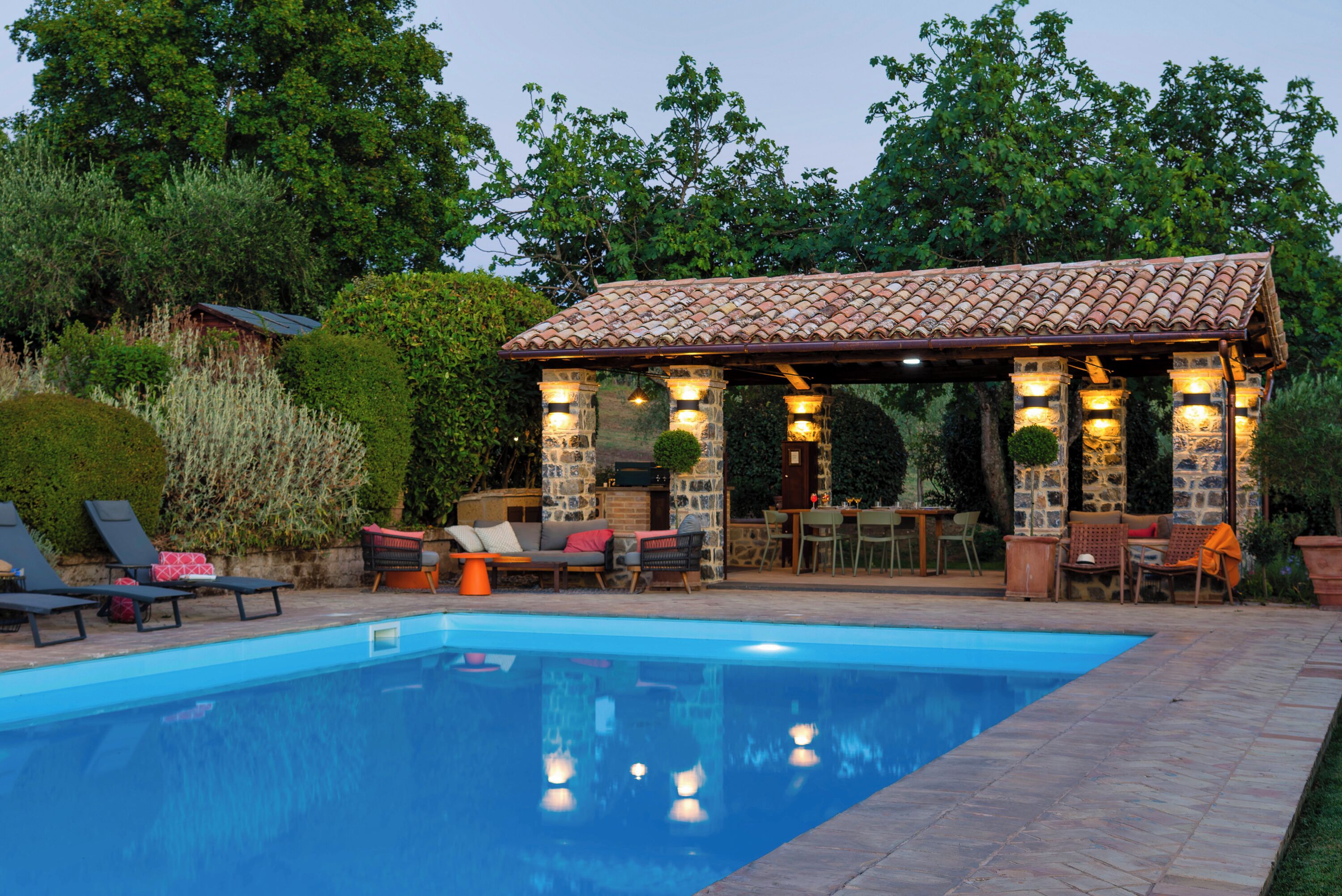 A pool area with a covered seating area, stone pillars, and lounge chairs.
