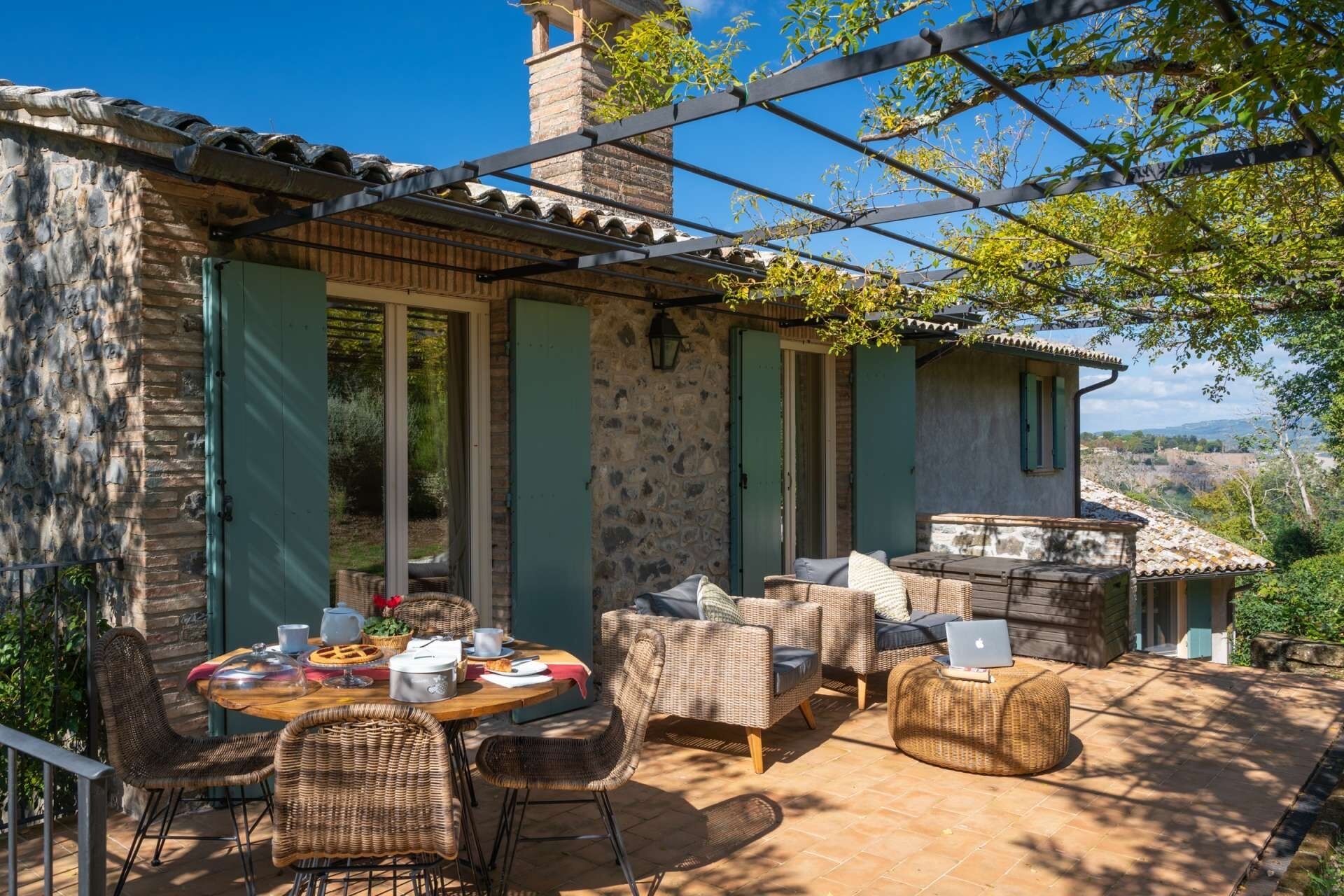 A stone building with a patio area featuring wicker furniture and a table set for dining.