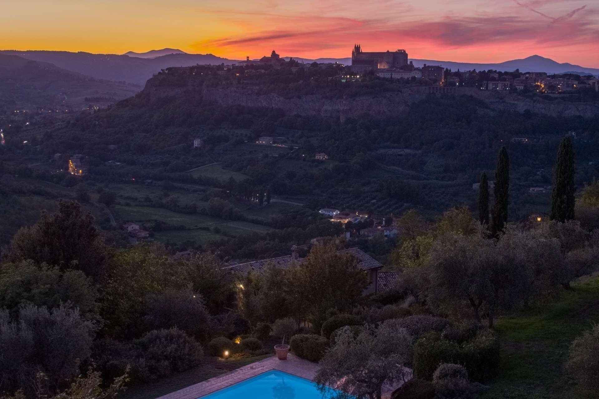 Vista panorámica de un pueblo histórico en una colina, con un castillo, rodeado de exuberante vegetación y una zona de piscina.