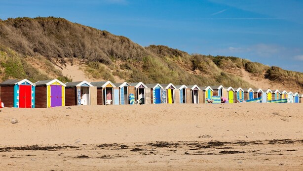 Une rangée de cabanes de plage, avec une plage de sable et des dunes en arrière-plan.