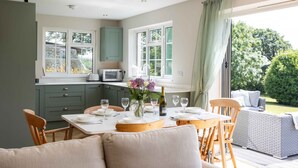 Une cuisine moderne avec des meubles de couleur verte, un coin repas avec une table dressée pour quatre personnes, et une vue sur le jardin grâce à de grandes fenêtres.