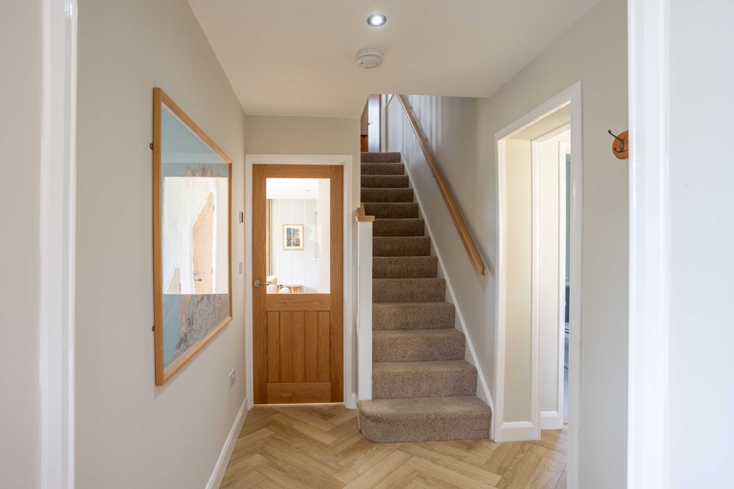 A hallway with a wooden door, a carpeted staircase, and a herringbone-patterned floor.
