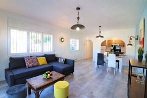A spacious living area with a sofa, ottoman, and a wooden coffee table. There is a dining area with a white table and chairs, and a kitchen in the background. - Apartment in Roses With Waterfront Views (Roses)