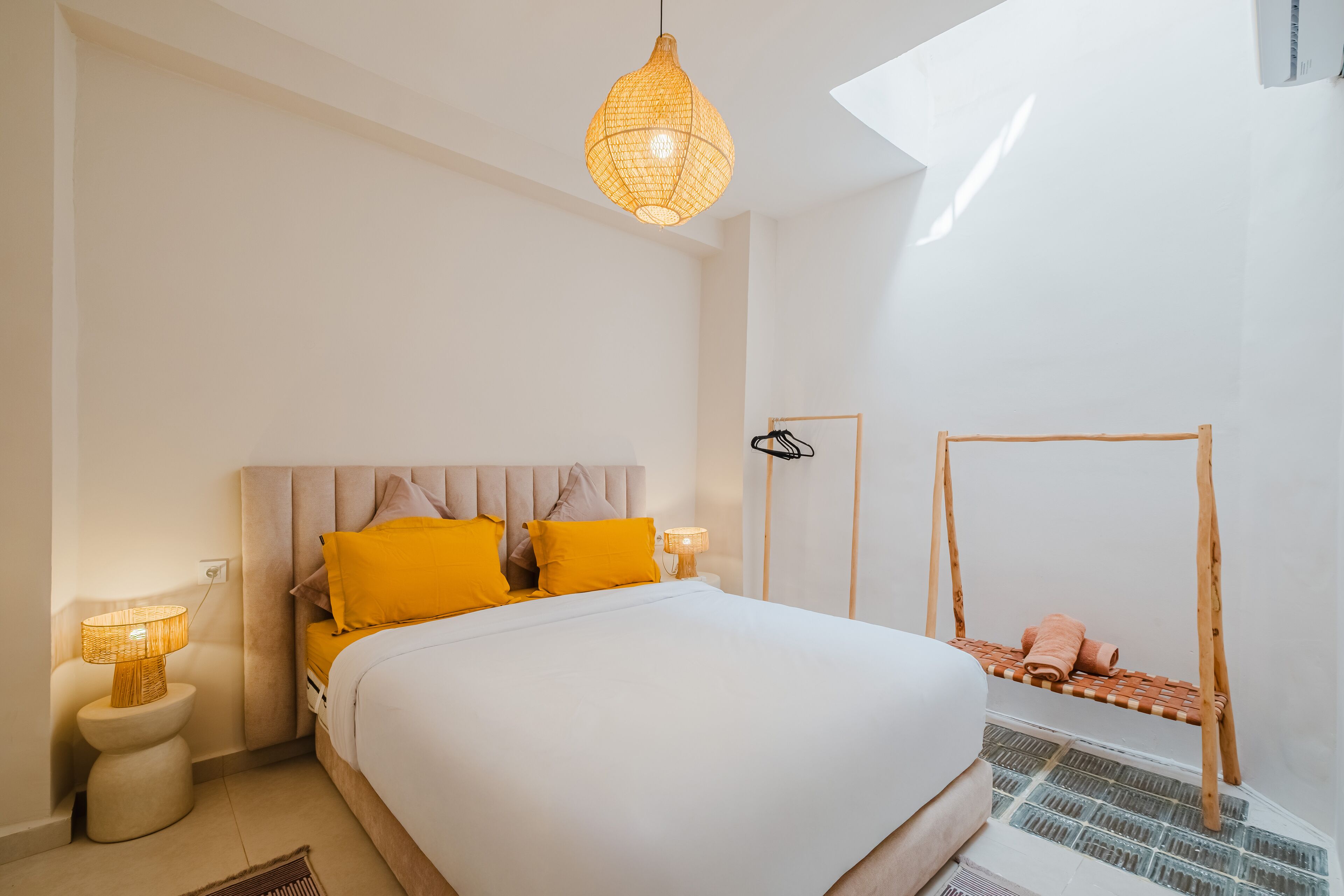 Une chambre avec un grand lit, un luminaire suspendu, une petite table de chevet et une étagère fixée au mur.