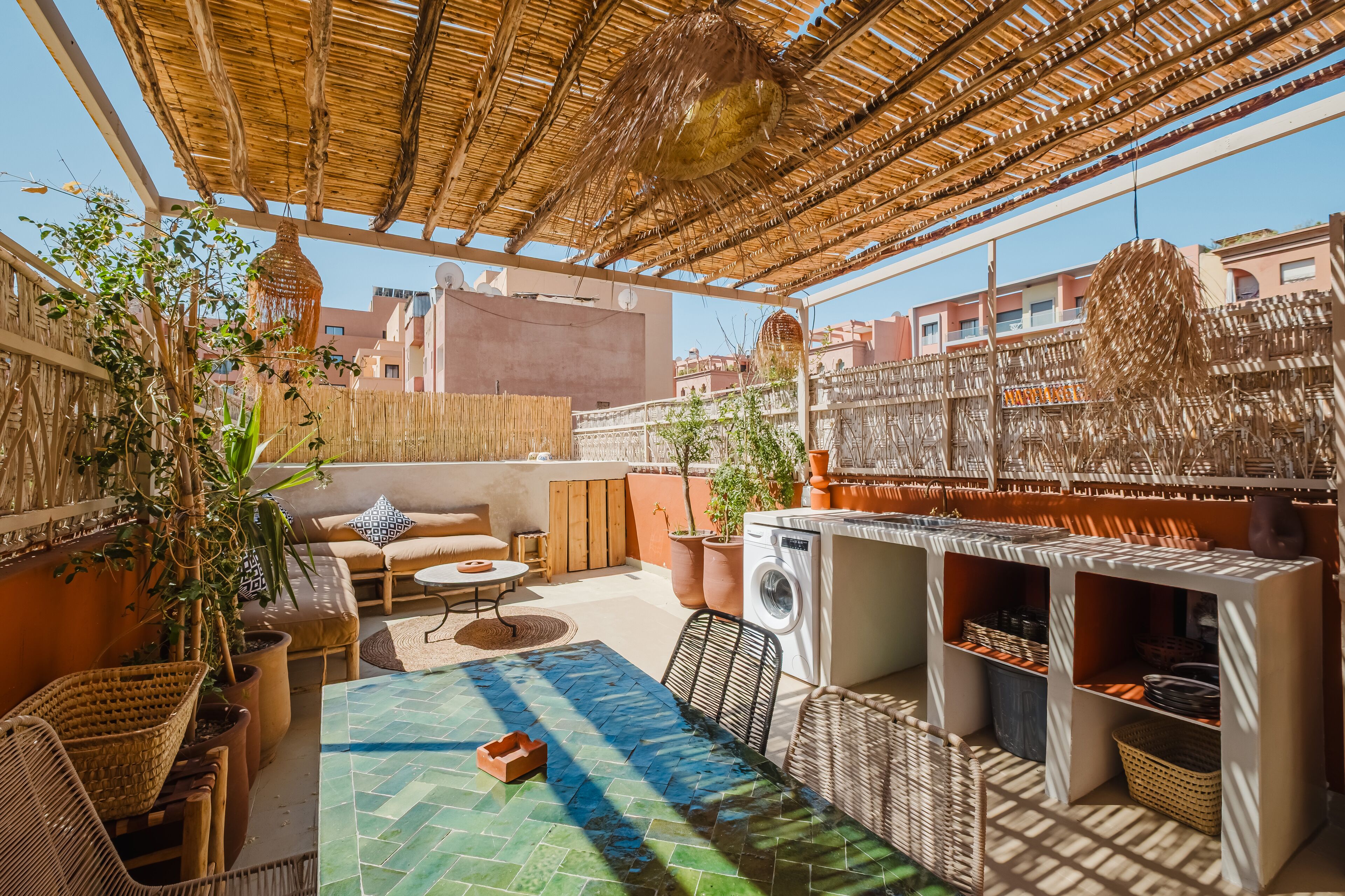 A rooftop patio with a woven ceiling, outdoor furniture, a washing machine, and potted plants.
