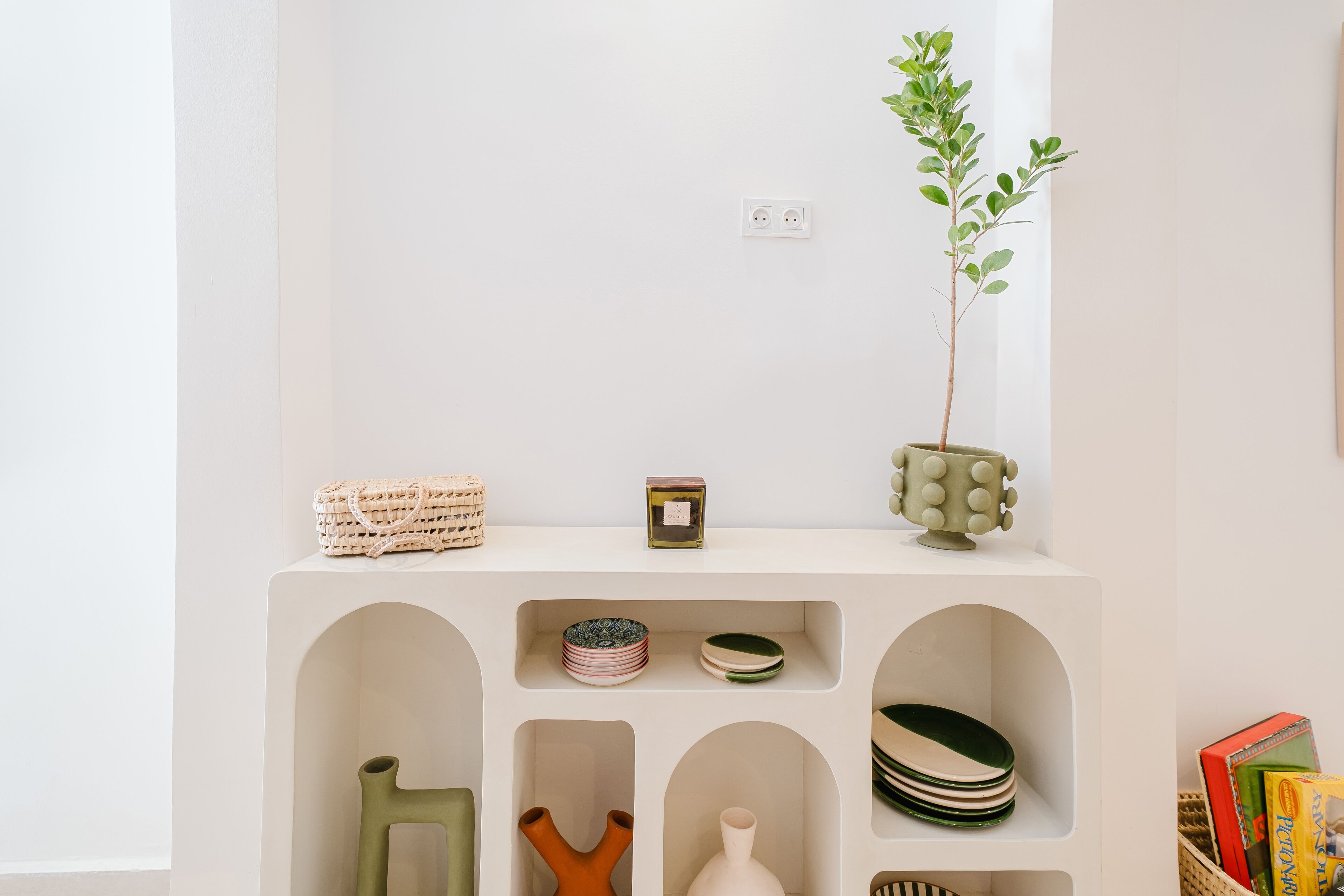 Une étagère minimaliste agrémentée de divers objets décoratifs et d’une plante en pot.