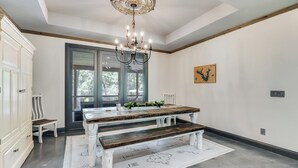 A dining area with a wooden table and bench, a chandelier, and a view through a glass door. - Refined Lake Retreat on Lake Fork in Emory, TX, fishing, kayaking, antiquing (Emory)