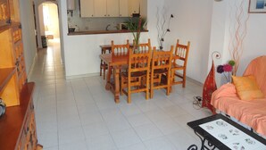 A dining area with a wooden table and chairs, a kitchen in the background, and a living area with a sofa and a clock on the wall. - Cozy Apartment With Furniture (Roses)