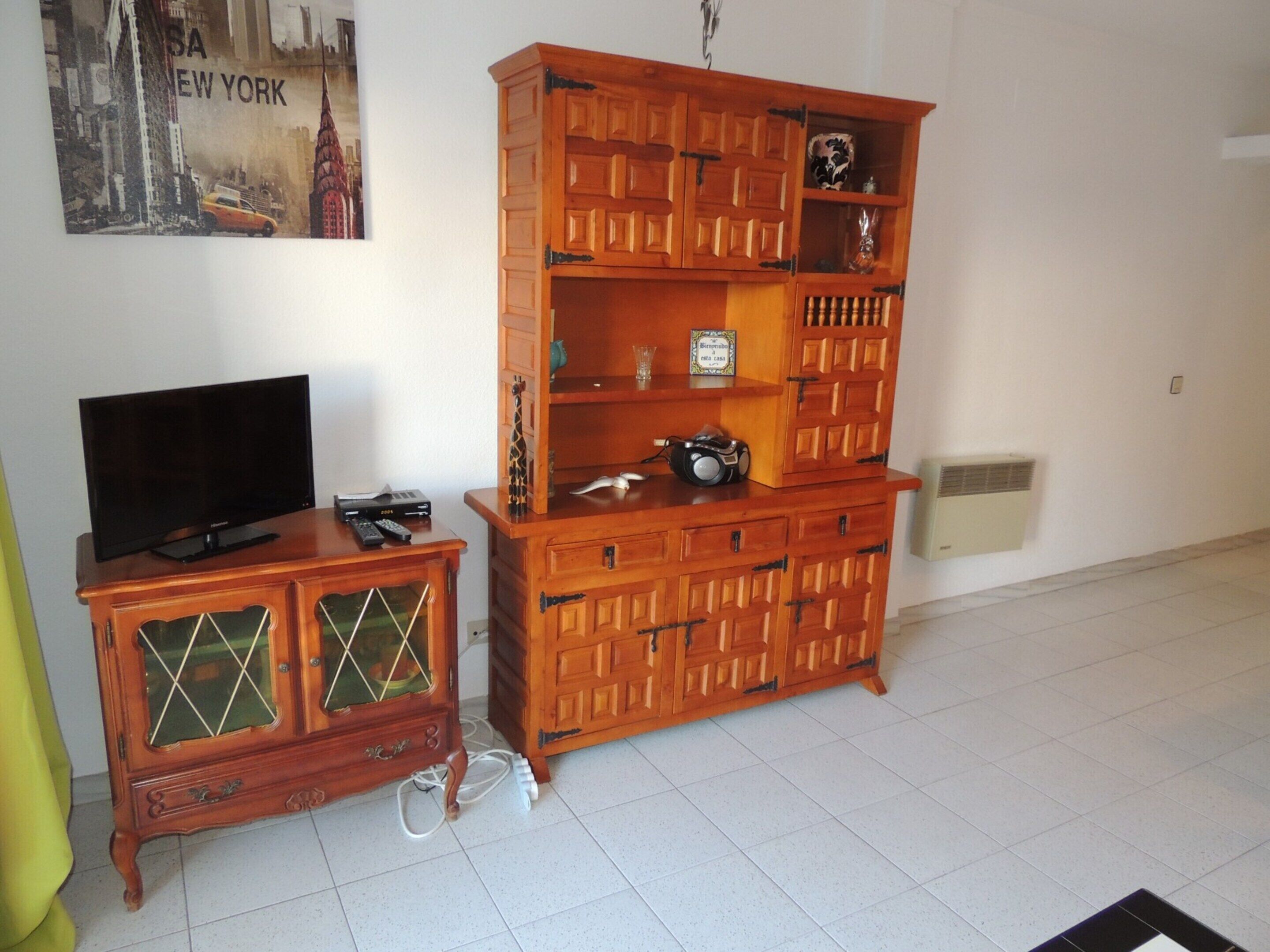 A living room with a wooden entertainment center, a television, and a poster of New York.