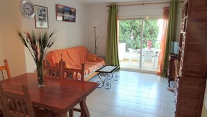 A living room with a wooden dining table, chairs, a sofa, a coffee table, a clock, and a framed picture on the wall. - Cozy Apartment With Furniture (Roses)